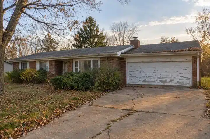 Brick ranch house with a worn garage door and cracked driveway